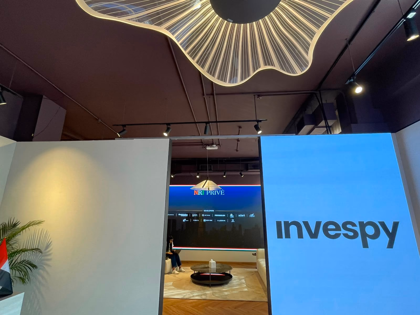 Looking up at the fluted, backlit sculptural ceiling light above the Broker Hub entrance, next to the illuminated Invespy wall.