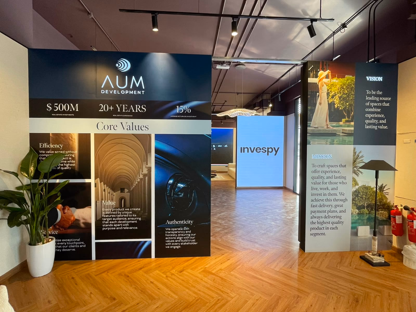 The exhibition walk lined with floor-to-ceiling developer display panels, leading toward the illuminated Invespy wall at the far end.
