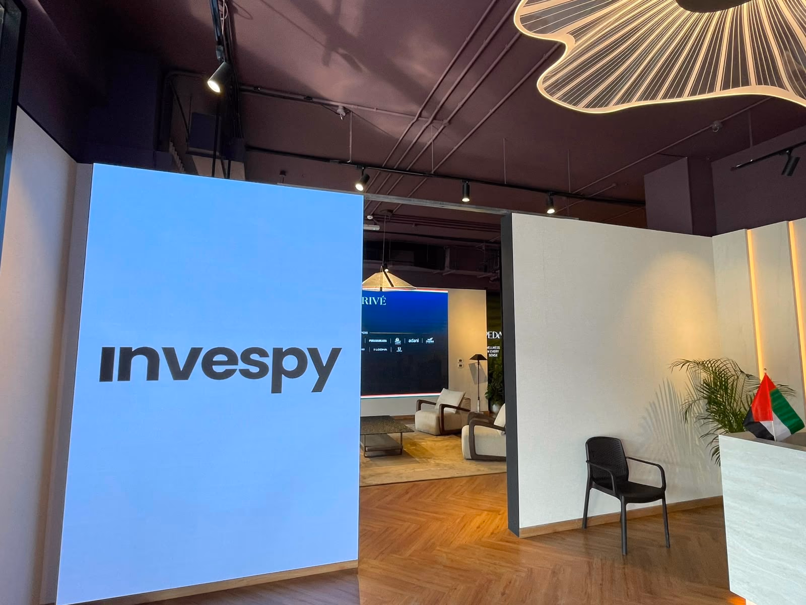 The Invespy-branded LED wall at the entrance to the Broker Hub, with a sculptural illuminated ceiling feature overhead and the lounge visible beyond.