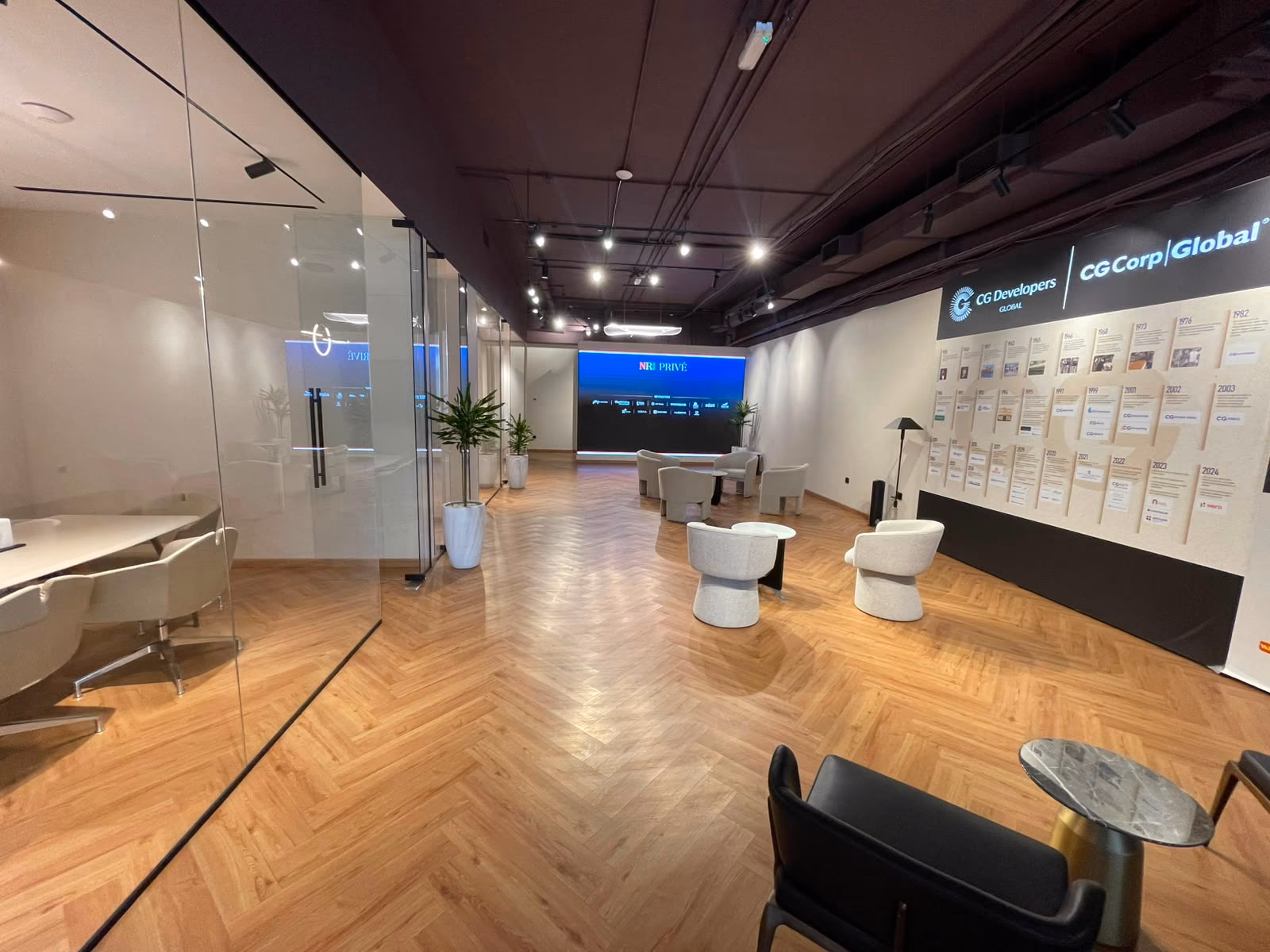 The main floor looking down the herringbone oak corridor, with a glass meeting room on the left and lounge seating around the LED display ahead.