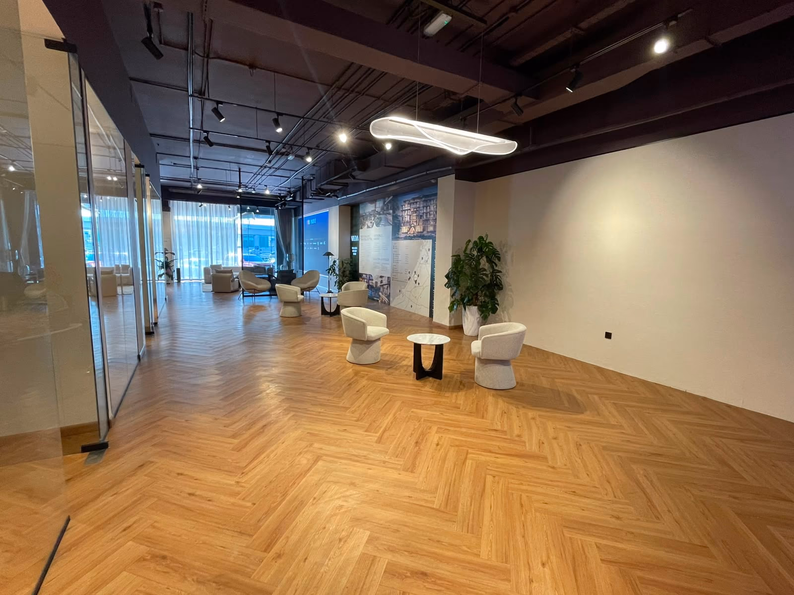An open breakout area with pale bouclé tub chairs around a small marble side table, under a curved linear pendant light.